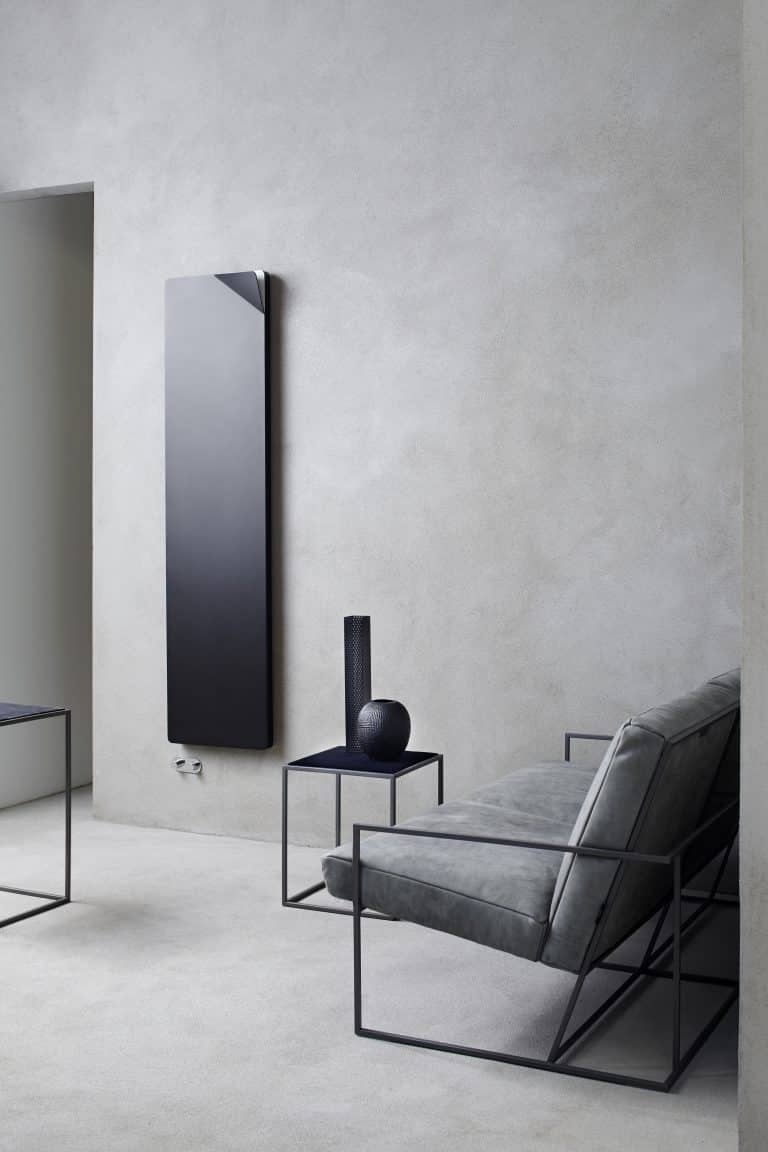 Betonová stěrka v obýváku, kovová křesla a stolek, černý designový radiátor na zdi