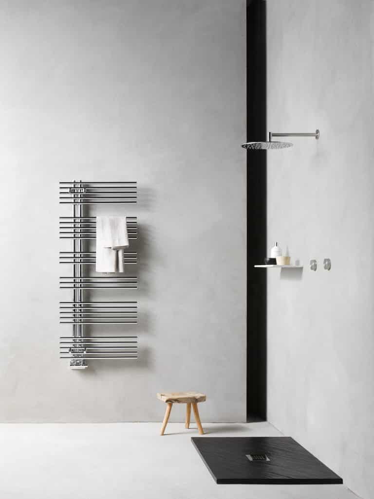Betonová stěrka v koupelně, dřevěná stolička, černá sprchová vanička a stříbrný lesklý radiátor