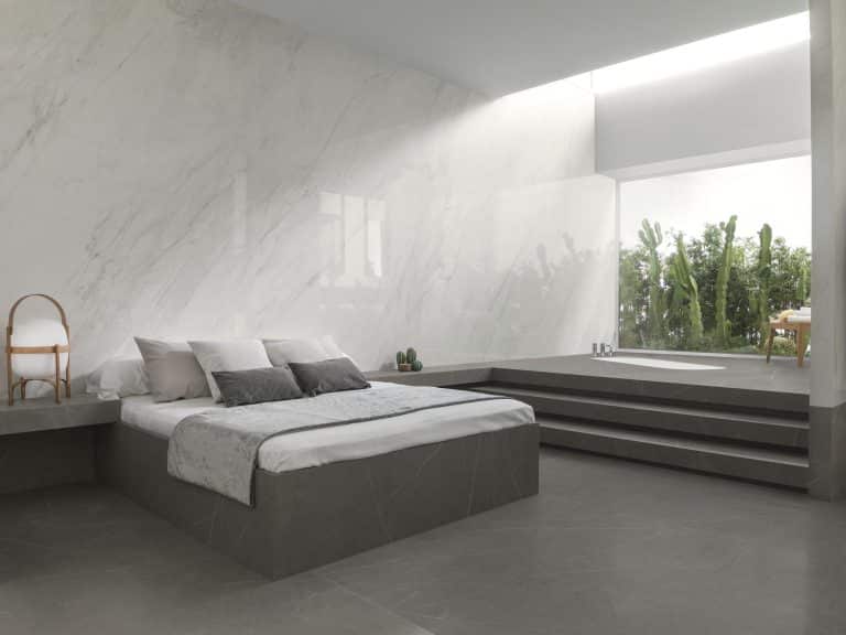 Ložnice s šedou manželskou postelí obloženou šedým mramorem, velkoformátová dlažba s imitací šedého mramoru, obklad na zdi z bílého mramoru