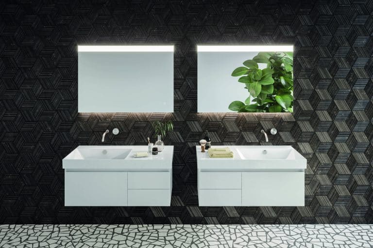 Tmavá koupelna s černou mozaikou na zdi, dvěma umyvadly, dvě bílé skříňky pod umyvadlo se zásuvkami,