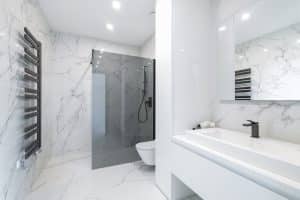 Bílá mramorová koupelna, sprchová zástěna typu walk-in, toaleta závěsná, černá sprchová souprava na tyči