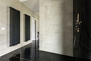Černá mramorová koupelna s velkoformátovým obkladem a dlažbou, černé radiátory, betonový obklad na zdi, zlatá sprchová baterie