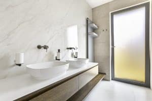 Bílá mramorová koupelna s velkoformátovým obkladem a dlažbou, oválná umyvadla na desce z umělého kamene, radiátor s poličkami na ručníky