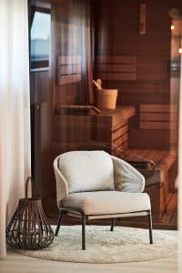 šedé designové křeslo, béžový kulatý kobereček, dřevěná dekorace, dřevěná sauna